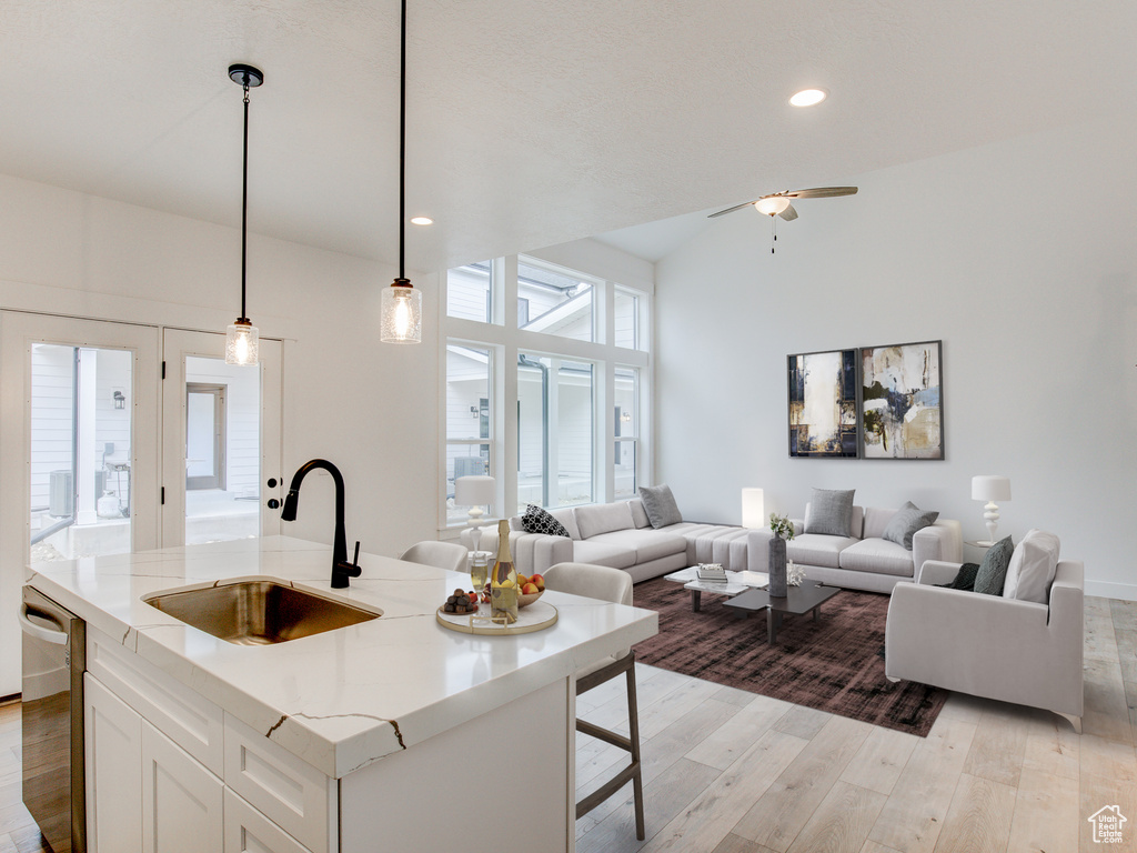 Kitchen with decorative light fixtures, a sink, white cabinets, open floor plan, and a center island with sink