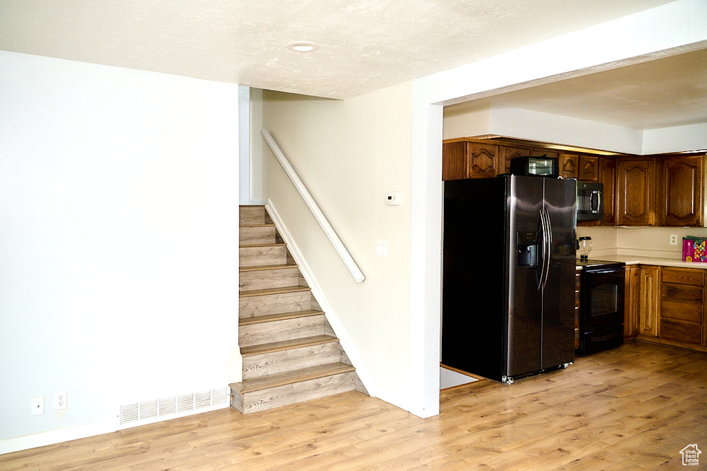 Kitchen featuring light wood finished floors, visible vents, light countertops, a textured ceiling, and black appliances