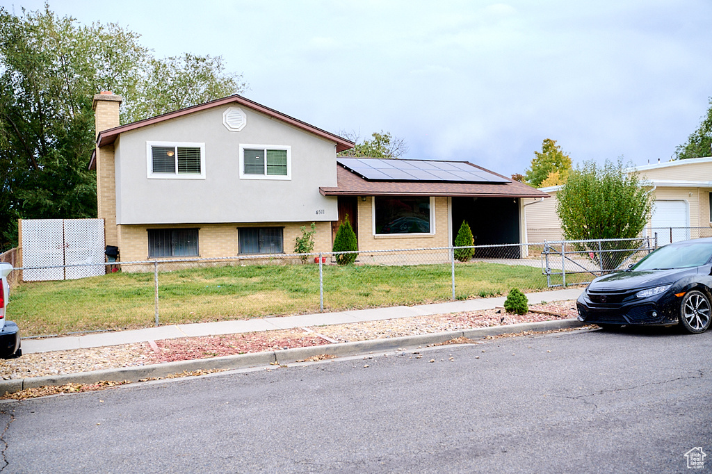 Split level home with fence private yard, brick siding, a front yard, and solar panels