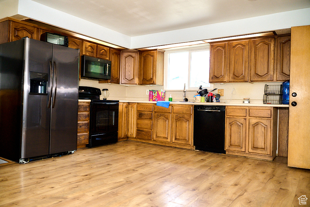 Kitchen with a sink, light wood-style floors, light countertops, brown cabinets, and black appliances
