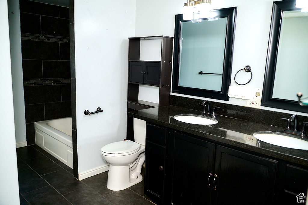 Bathroom with double vanity, a sink, toilet, and tile patterned floors