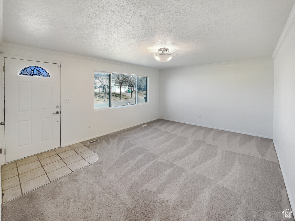 Entryway featuring visible vents, crown molding, baseboards, a textured ceiling, and light colored carpet