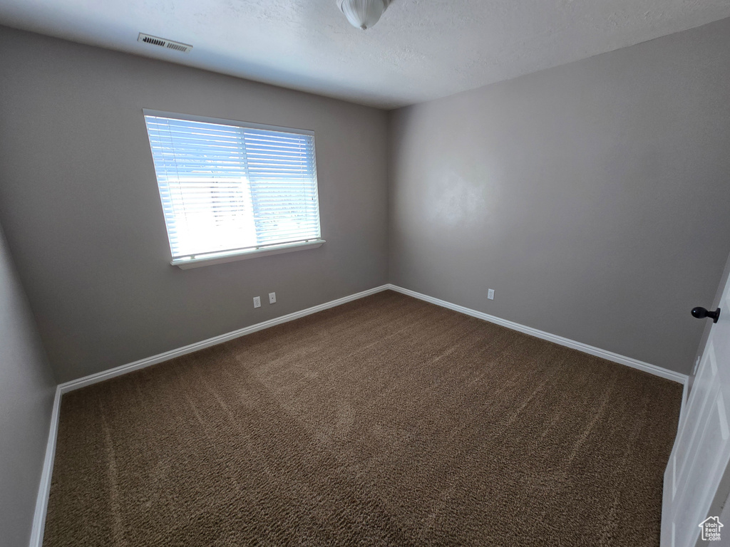 Empty room with dark carpet, visible vents, baseboards, and a textured ceiling