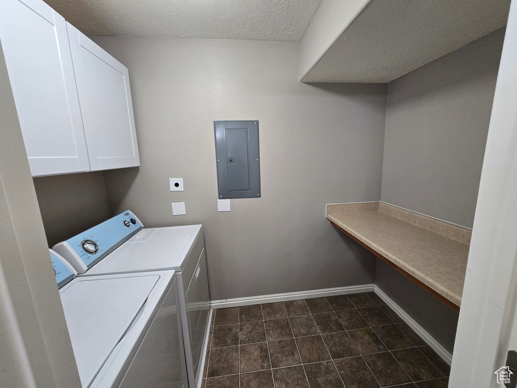 Laundry room with baseboards, electric panel, a textured ceiling, cabinet space, and washer and dryer