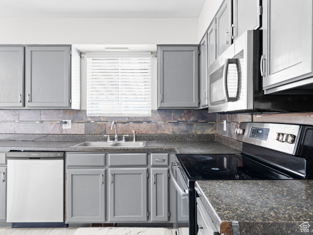 Kitchen featuring stainless steel appliances, decorative backsplash, a sink, and gray cabinetry