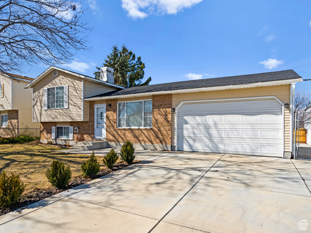 Split level home featuring a garage, concrete driveway, brick siding, and a chimney