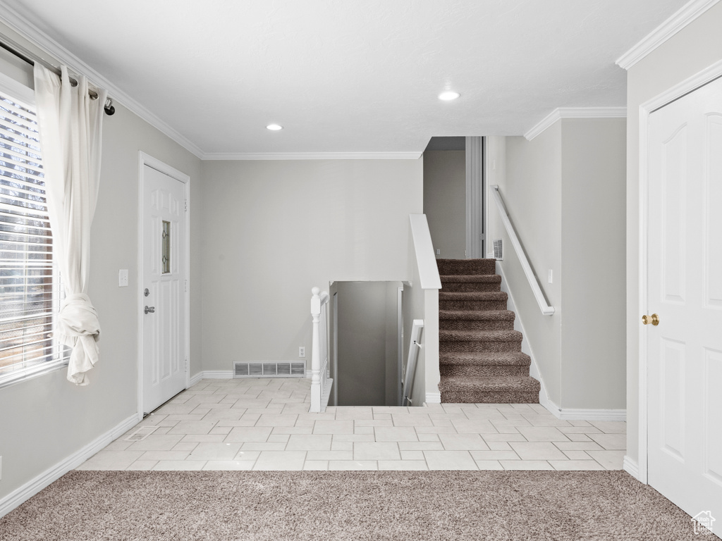 Entrance foyer featuring crown molding, visible vents, and light colored carpet