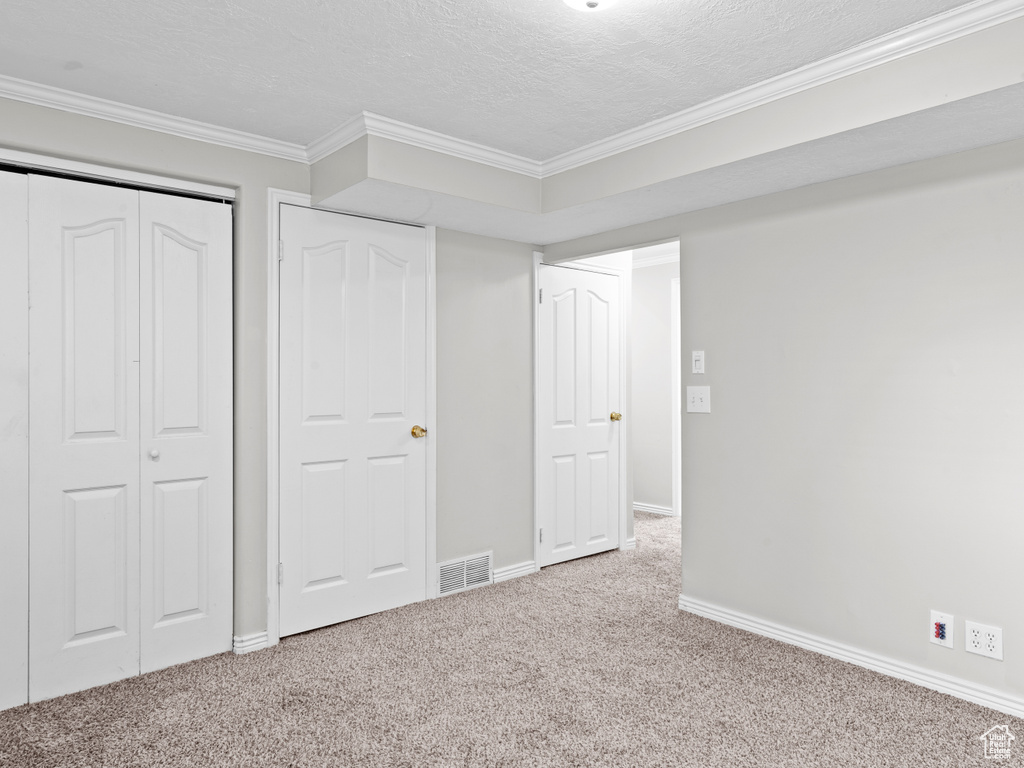 Unfurnished bedroom with a textured ceiling, light colored carpet, visible vents, baseboards, and ornamental molding