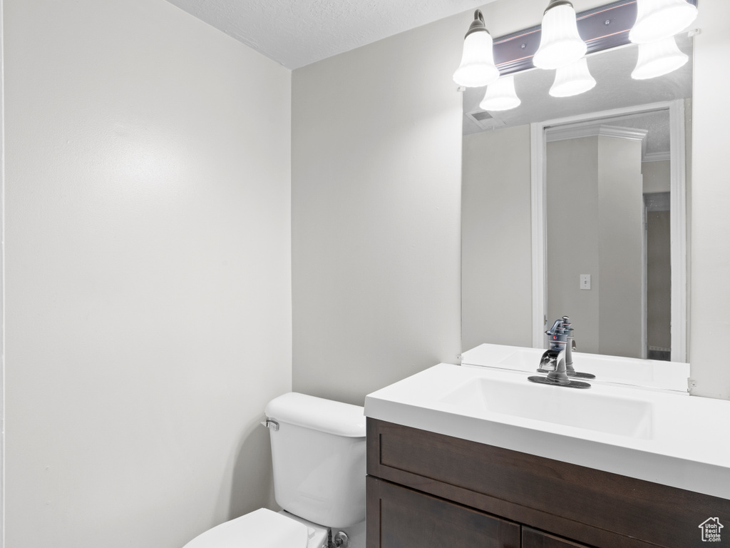 Half bath featuring visible vents, vanity, toilet, and a textured ceiling