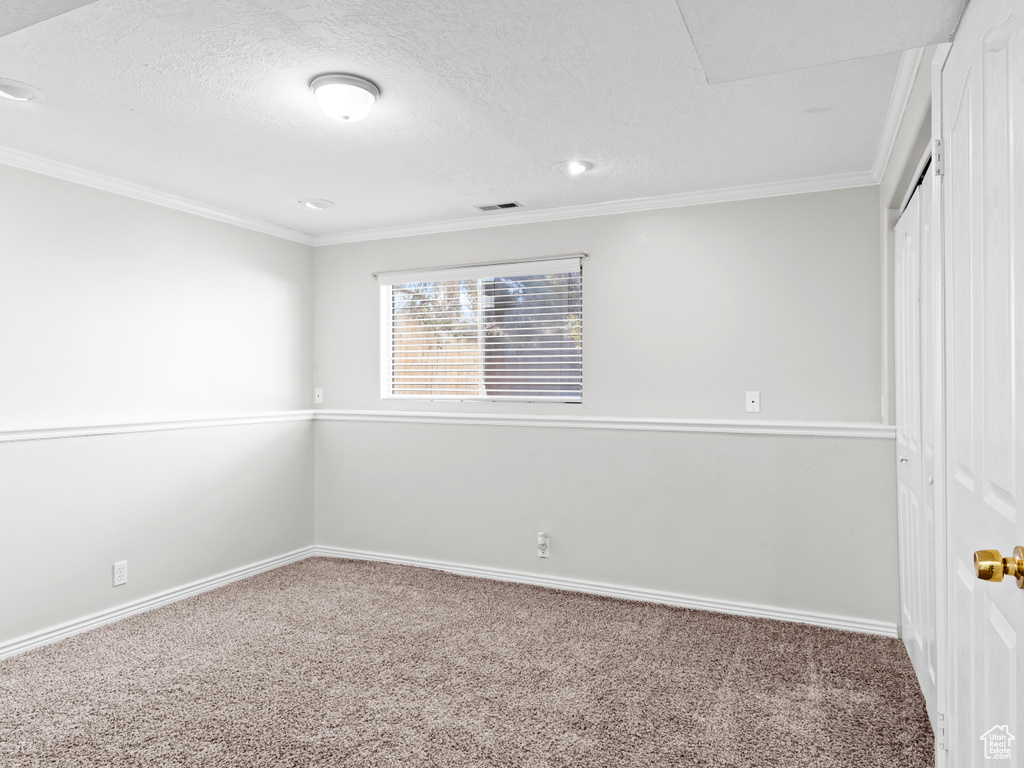 Unfurnished bedroom featuring a textured ceiling, carpet flooring, visible vents, baseboards, and crown molding