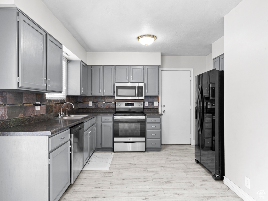 Kitchen with dark countertops, backsplash, gray cabinetry, appliances with stainless steel finishes, and a sink