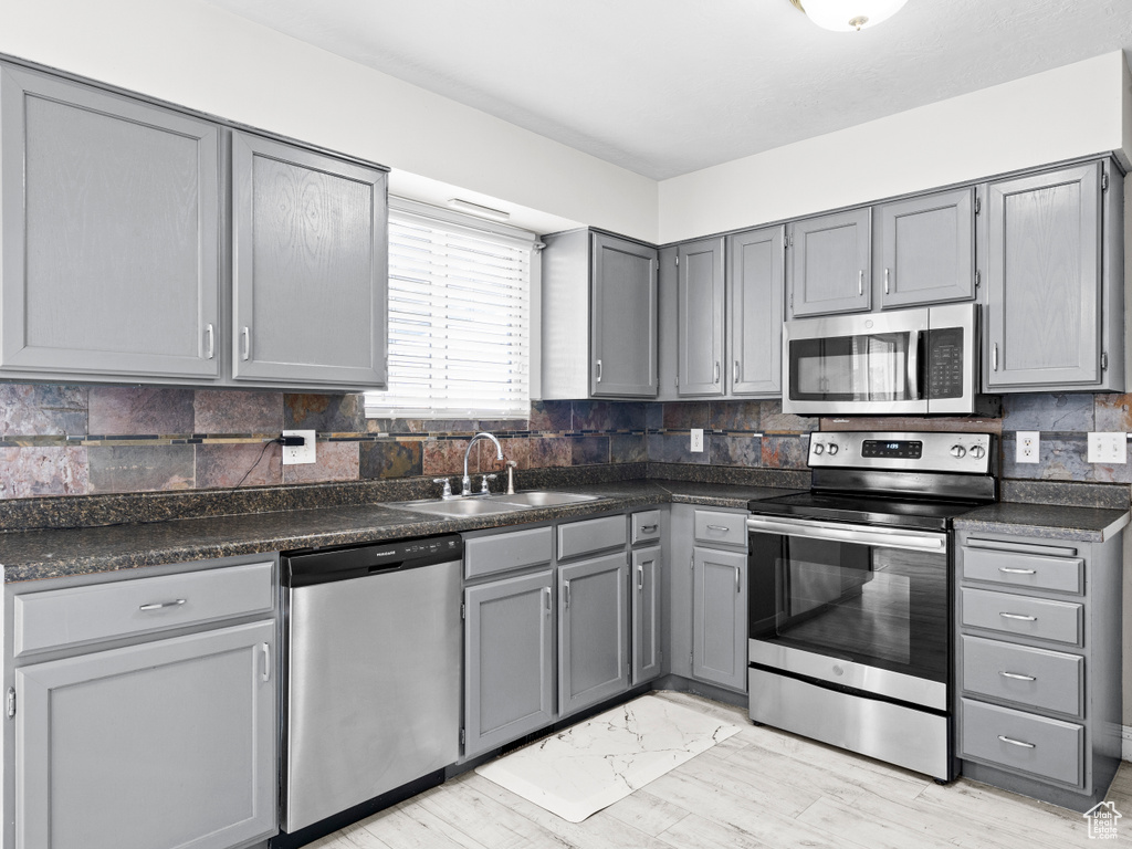 Kitchen featuring stainless steel appliances, dark countertops, gray cabinets, decorative backsplash, and a sink