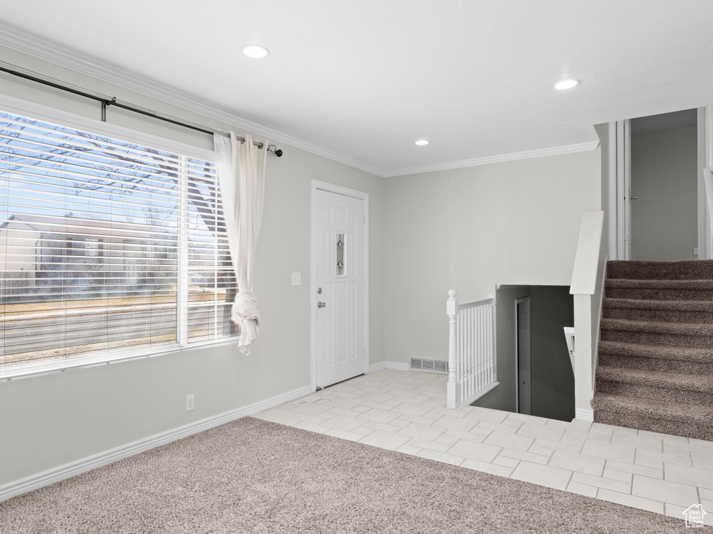 Foyer with crown molding, visible vents, light carpet, light tile patterned flooring, and stairs