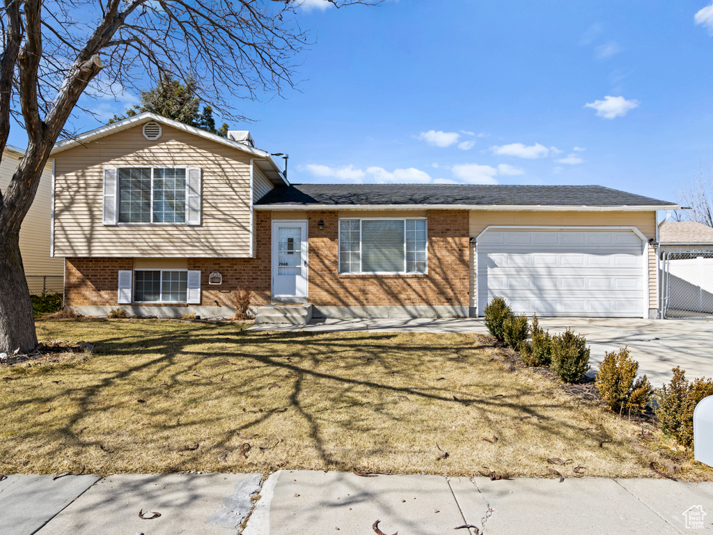 Tri-level home with brick siding, concrete driveway, a front yard, entry steps, and a garage