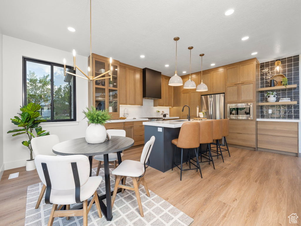 Kitchen featuring pendant lighting, a center island with sink, stainless steel appliances, light countertops, and glass insert cabinets