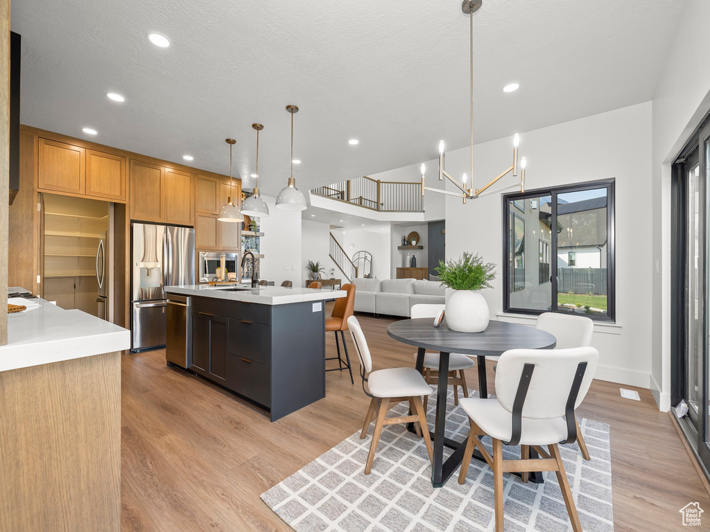 Kitchen with stainless steel appliances, open floor plan, light countertops, an island with sink, and pendant lighting