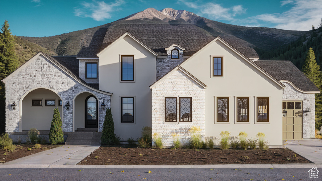 French country style house with stone siding, roof with shingles, and a mountain view