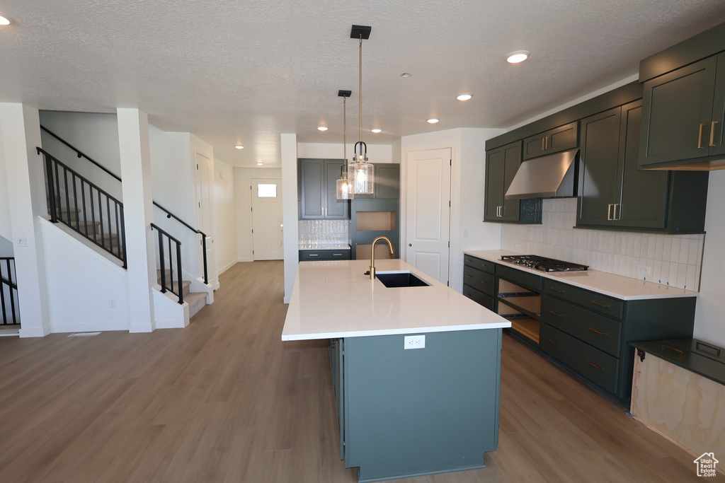 Kitchen featuring light wood-style flooring, a sink, tasteful backsplash, stainless steel gas stovetop, and under cabinet range hood