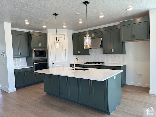 Kitchen featuring range hood, backsplash, a sink, baseboards, and appliances with stainless steel finishes