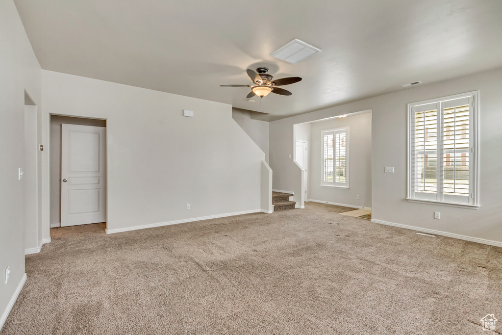 Spare room with a ceiling fan, light carpet, baseboards, and stairs