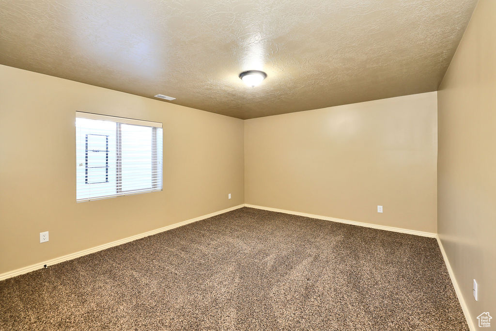 Spare room featuring carpet flooring, visible vents, baseboards, and a textured ceiling