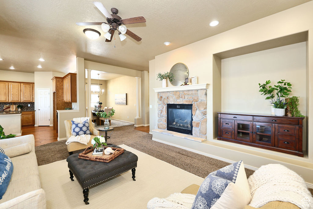 Living area with a textured ceiling, a stone fireplace, recessed lighting, a ceiling fan, and baseboards