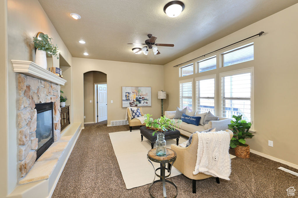 Living area featuring baseboards, arched walkways, a textured ceiling, a fireplace, and dark carpet