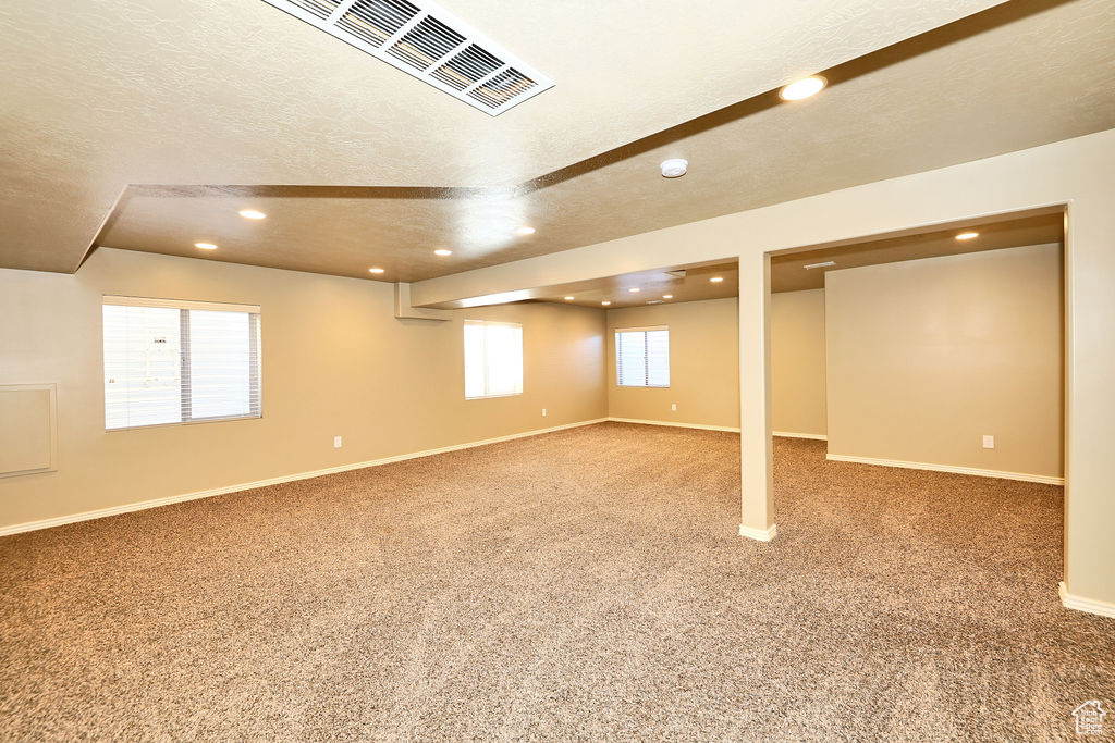 Basement with carpet floors, baseboards, visible vents, and a textured ceiling