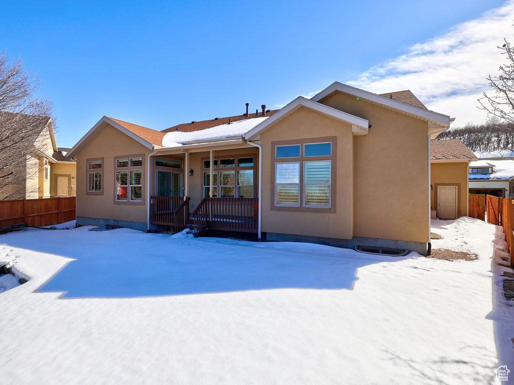 Snow covered rear of property with a porch, fence, and stucco siding