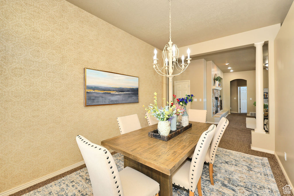Carpeted dining room featuring arched walkways, decorative columns, a chandelier, baseboards, and wallpapered walls