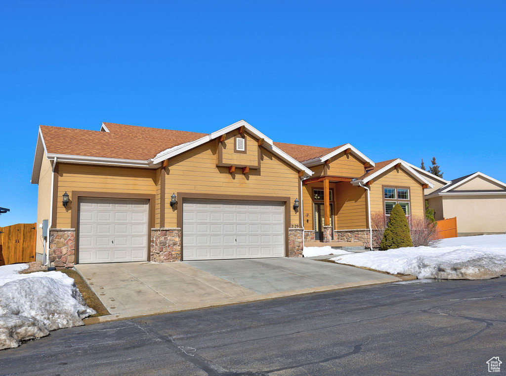 View of front of property featuring an attached garage, stone siding, a shingled roof, and concrete driveway