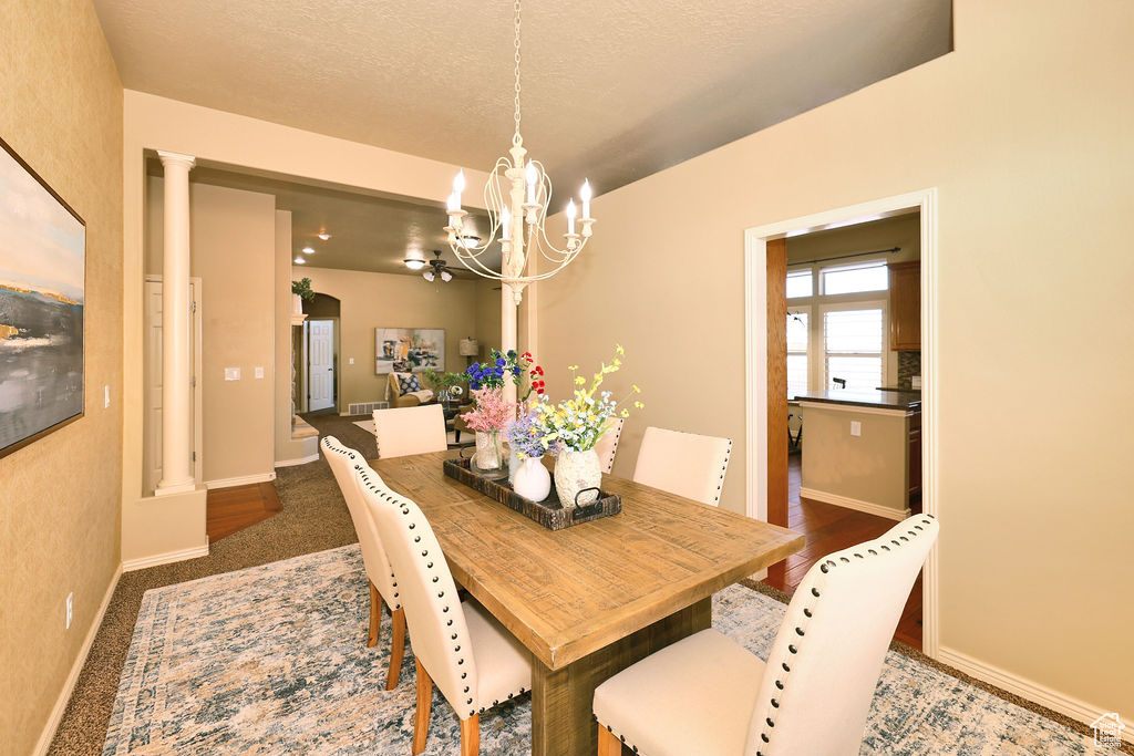 Dining space with baseboards, an inviting chandelier, a textured ceiling, ornate columns, and dark carpet