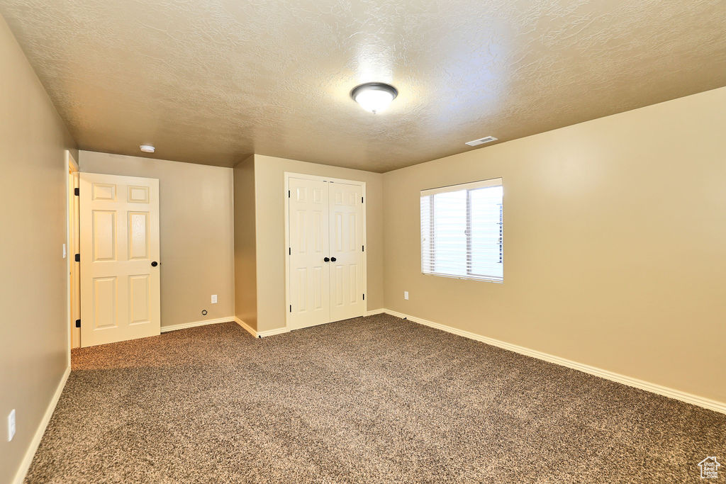 Spare room with a textured ceiling, carpet floors, visible vents, and baseboards