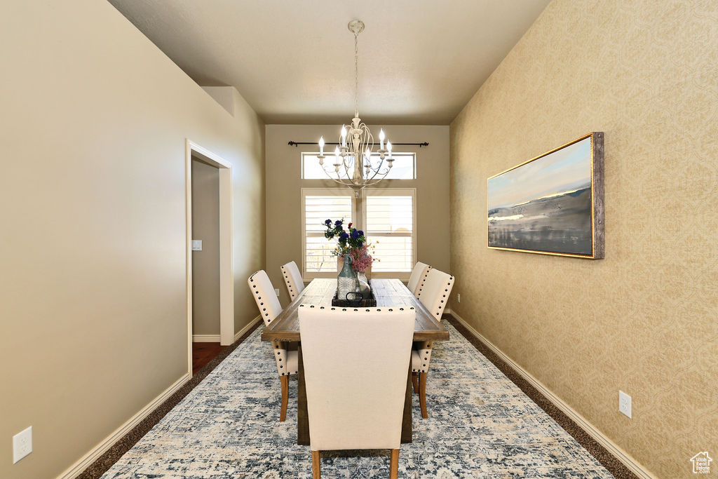 Dining area with wallpapered walls, baseboards, an accent wall, and a chandelier