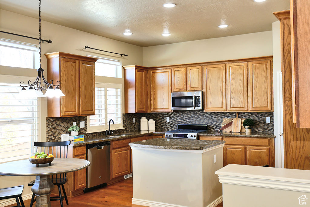 Kitchen featuring brown cabinets, decorative light fixtures, stainless steel appliances, a sink, and a kitchen island
