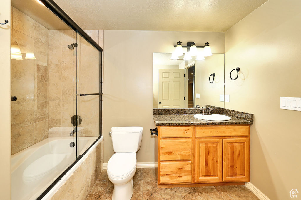 Bathroom with toilet, baseboards, combined bath / shower with glass door, and vanity