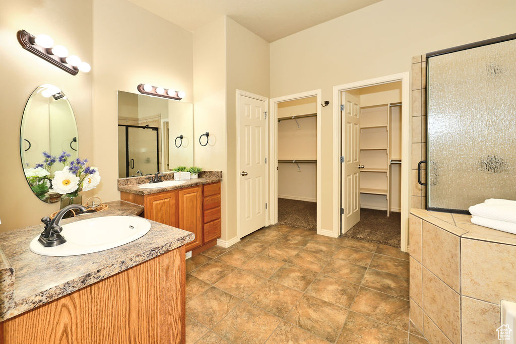 Bathroom featuring a shower stall, two vanities, a walk in closet, and a sink