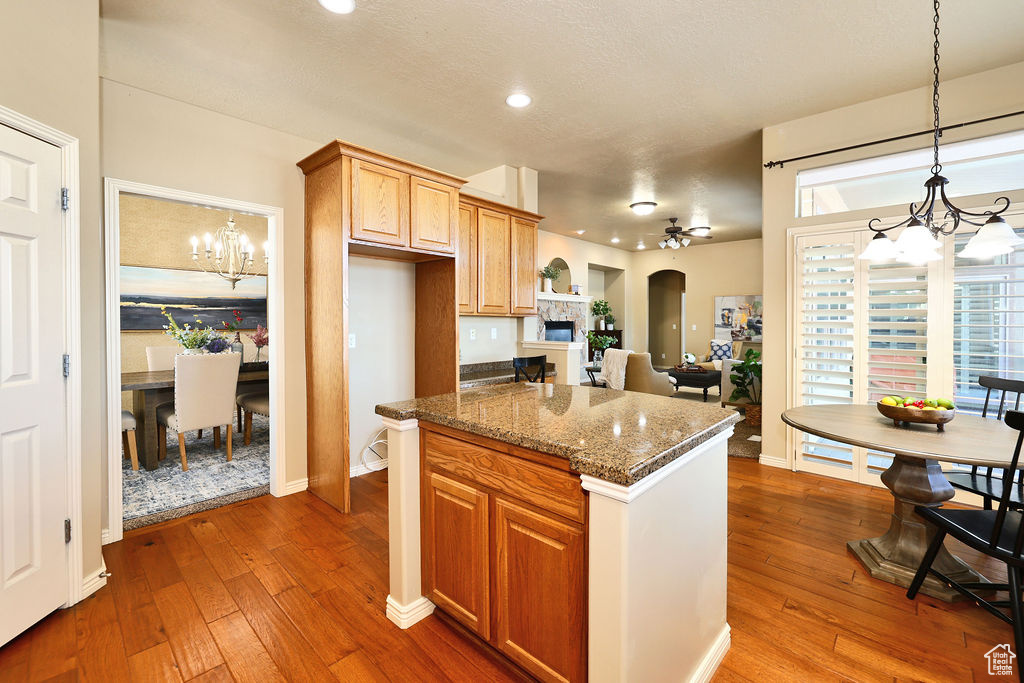 Kitchen with dark stone counters, hanging light fixtures, arched walkways, and wood finished floors