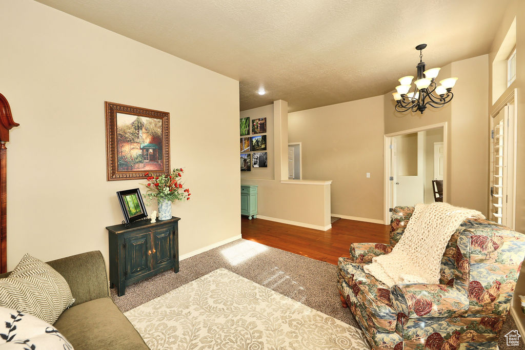 Living room with baseboards, a textured ceiling, wood finished floors, and a notable chandelier