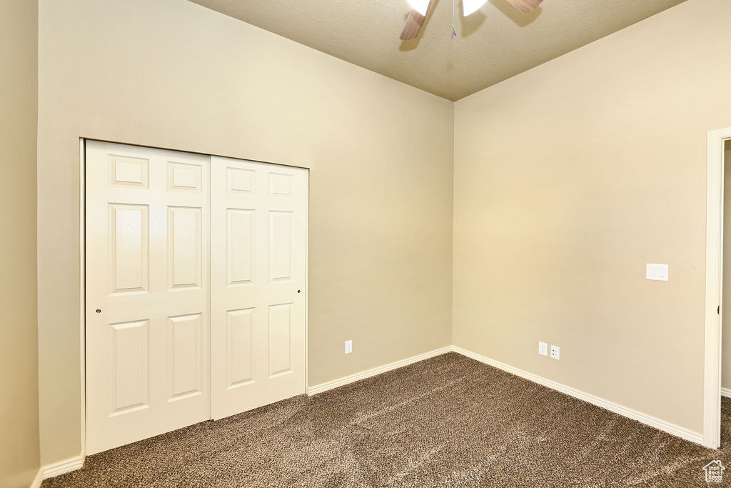 Unfurnished bedroom with dark colored carpet, a ceiling fan, and baseboards