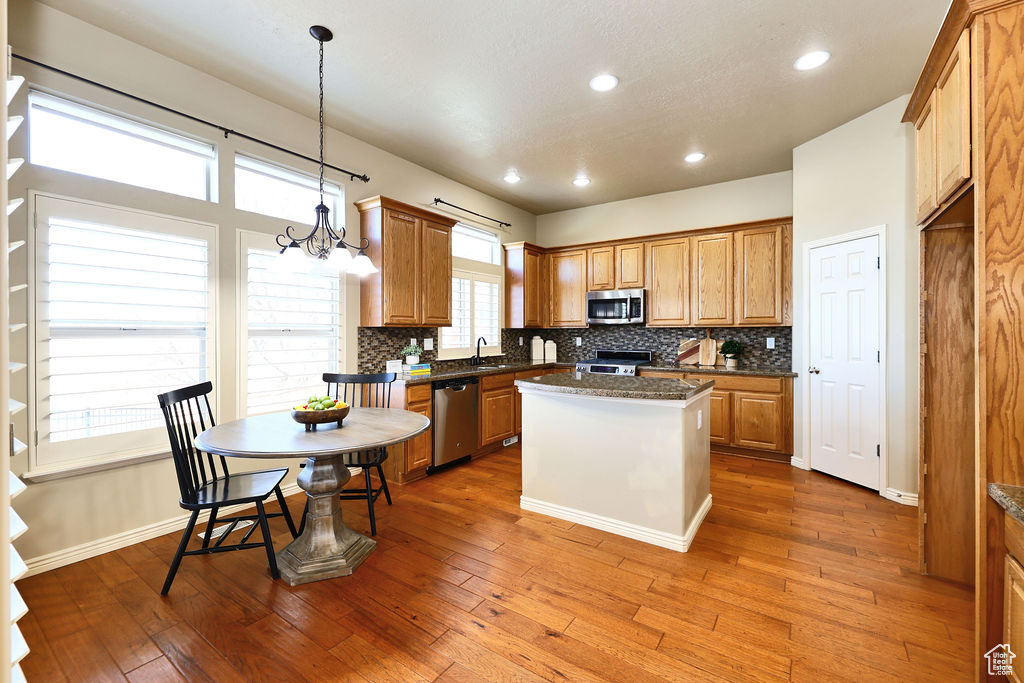 Kitchen featuring a kitchen island, appliances with stainless steel finishes, brown cabinets, wood finished floors, and pendant lighting