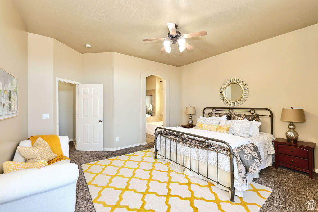 Bedroom with arched walkways, dark carpet, ensuite bathroom, ceiling fan, and baseboards