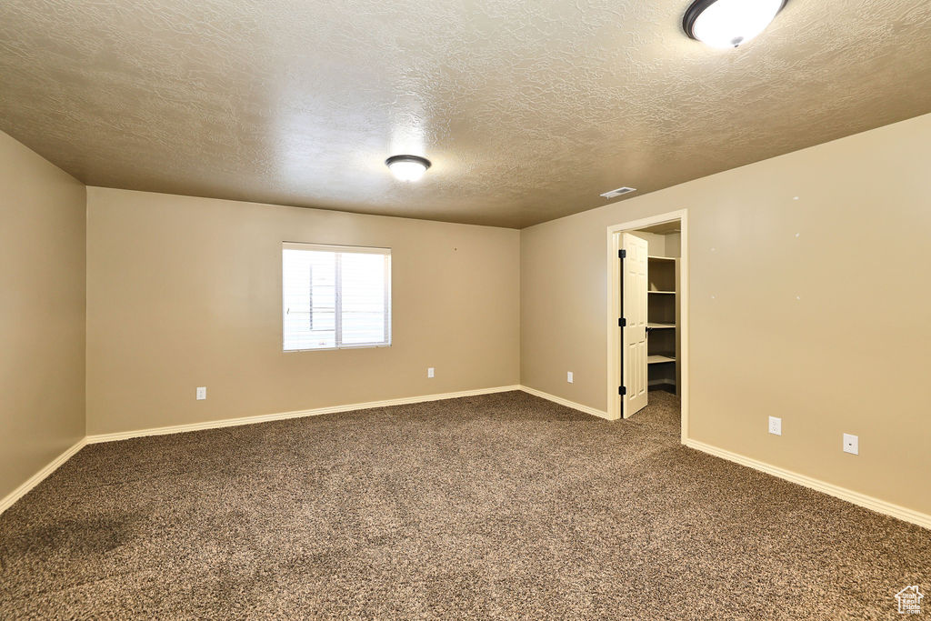 Spare room with a textured ceiling, carpet floors, visible vents, and baseboards