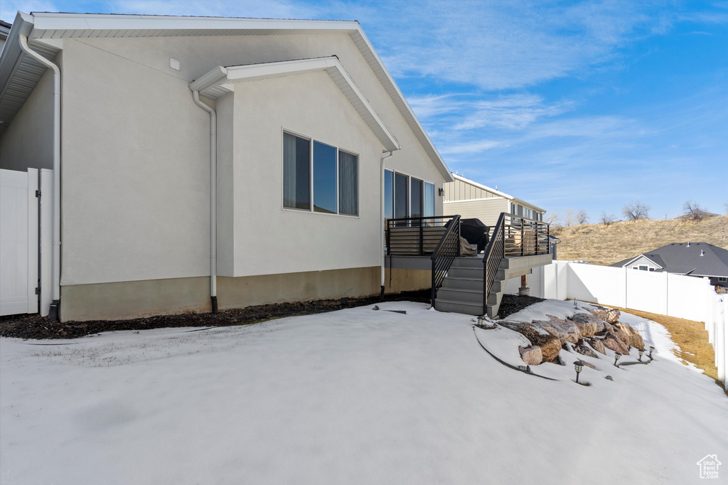 View of snowy exterior featuring a wooden deck, stairs, fence, and stucco siding