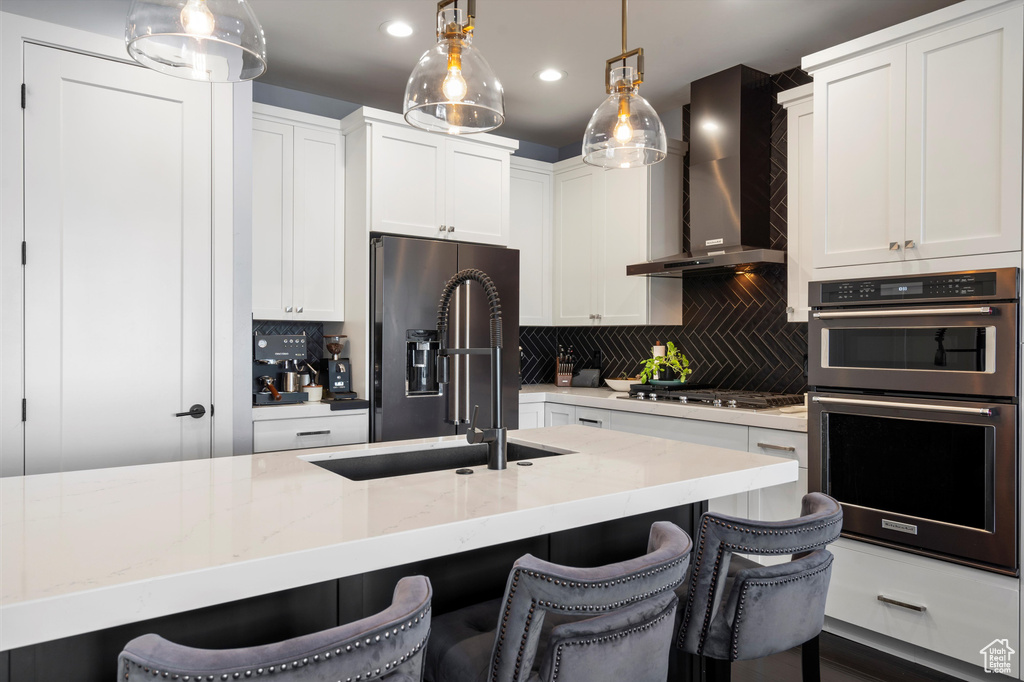 Kitchen featuring hanging light fixtures, wall chimney range hood, double wall oven, and refrigerator with ice dispenser