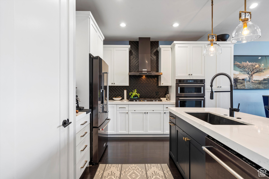 Kitchen with a sink, white cabinets, hanging light fixtures, appliances with stainless steel finishes, and wall chimney exhaust hood