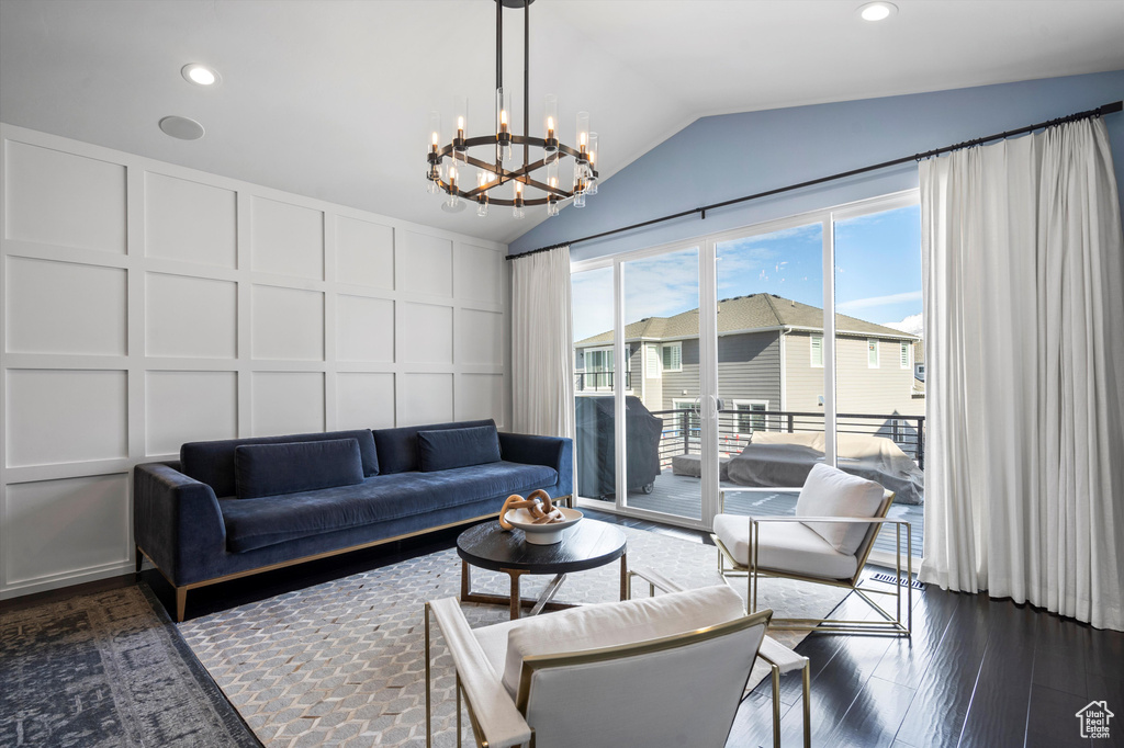 Living area with dark wood finished floors, a notable chandelier, lofted ceiling, recessed lighting, and a decorative wall