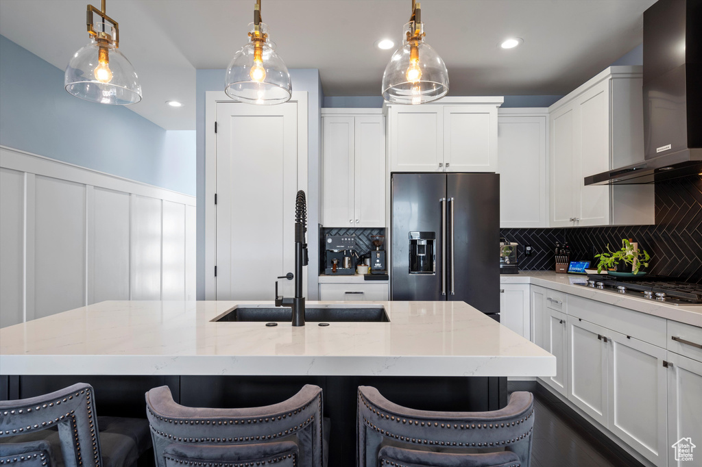Kitchen with stainless steel appliances, a breakfast bar, decorative light fixtures, and wall chimney range hood