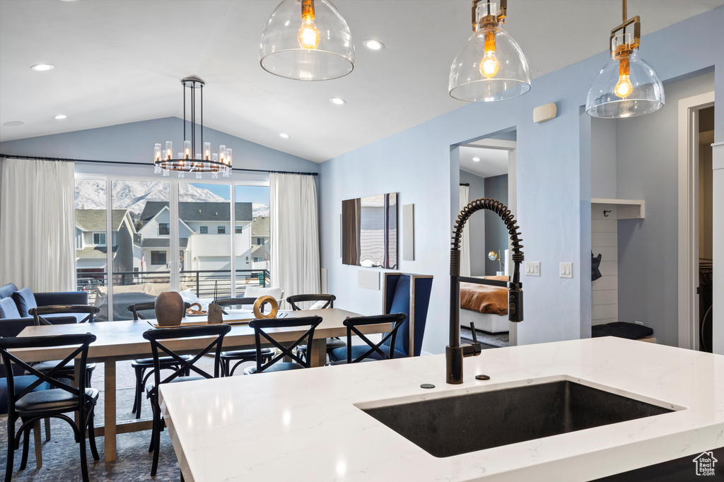 Kitchen featuring open floor plan, decorative light fixtures, light stone countertops, vaulted ceiling, and a sink