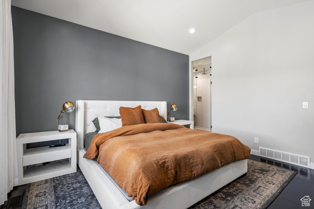 Bedroom featuring dark wood-style floors, visible vents, and vaulted ceiling